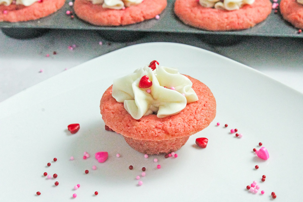 Pink Valentine sugar cookie cup topped with vanilla frosting on a white plate.