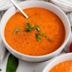 Bowl of vegan roasted tomato basil soup topped with fresh basil and black pepper.