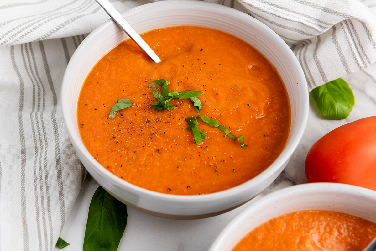 Bowl of vegan roasted tomato basil soup topped with fresh basil and black pepper.