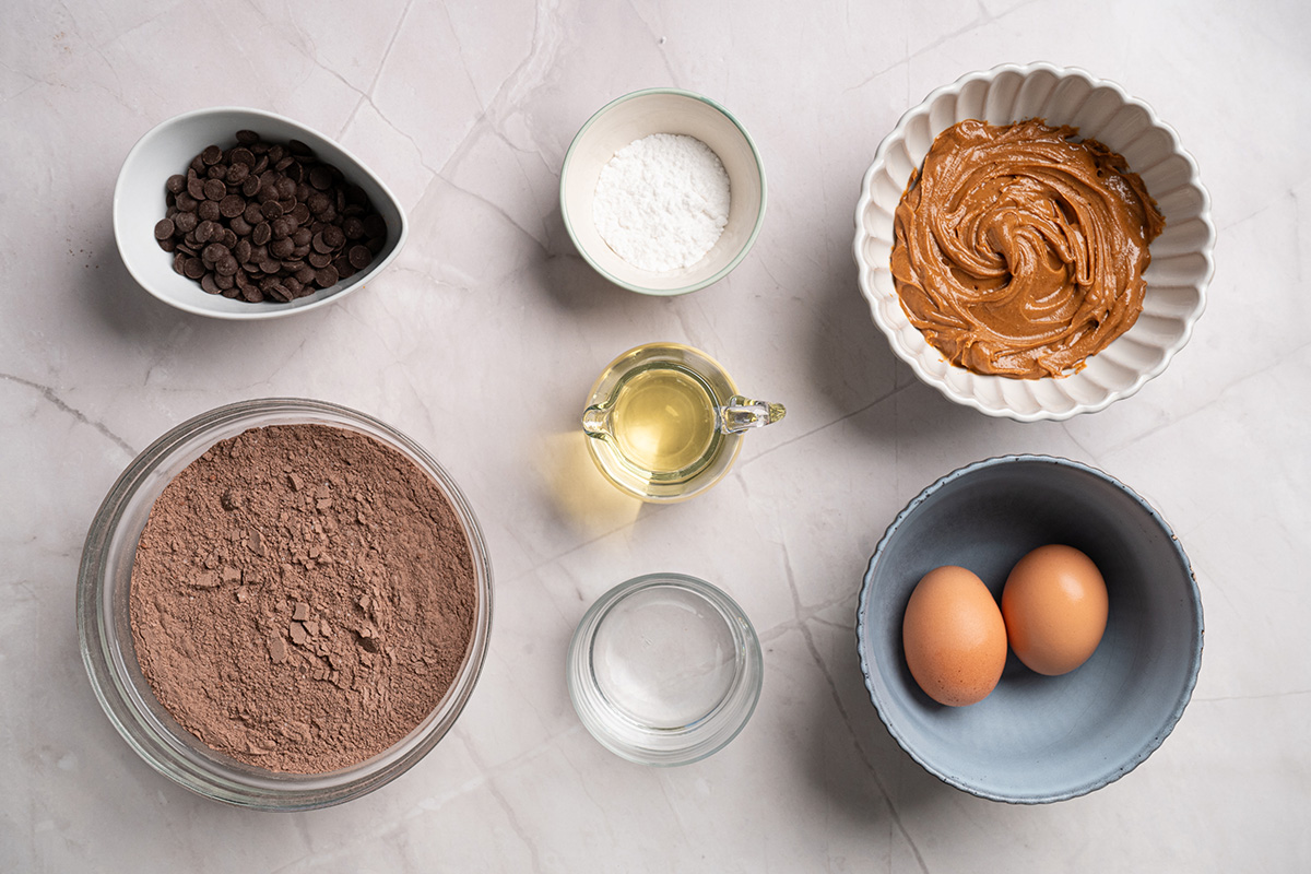 Ingredients for chocolate peanut butter swirl brownies including fudge brownie mix, eggs, oil, water, chocolate chips, creamy peanut butter, and powdered sugar.