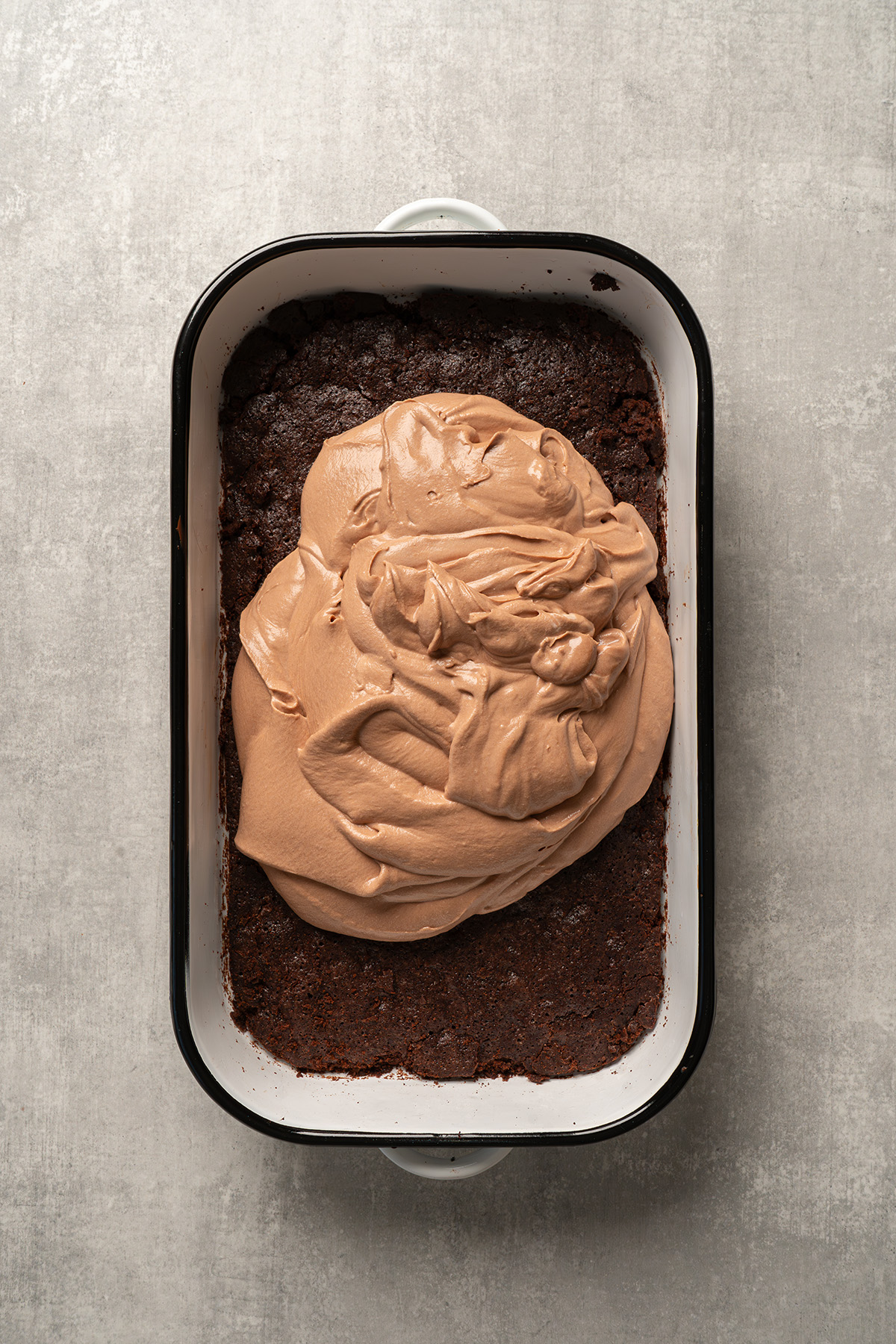 Chocolate French silk filling spread over a cooled brownie base in a baking dish.