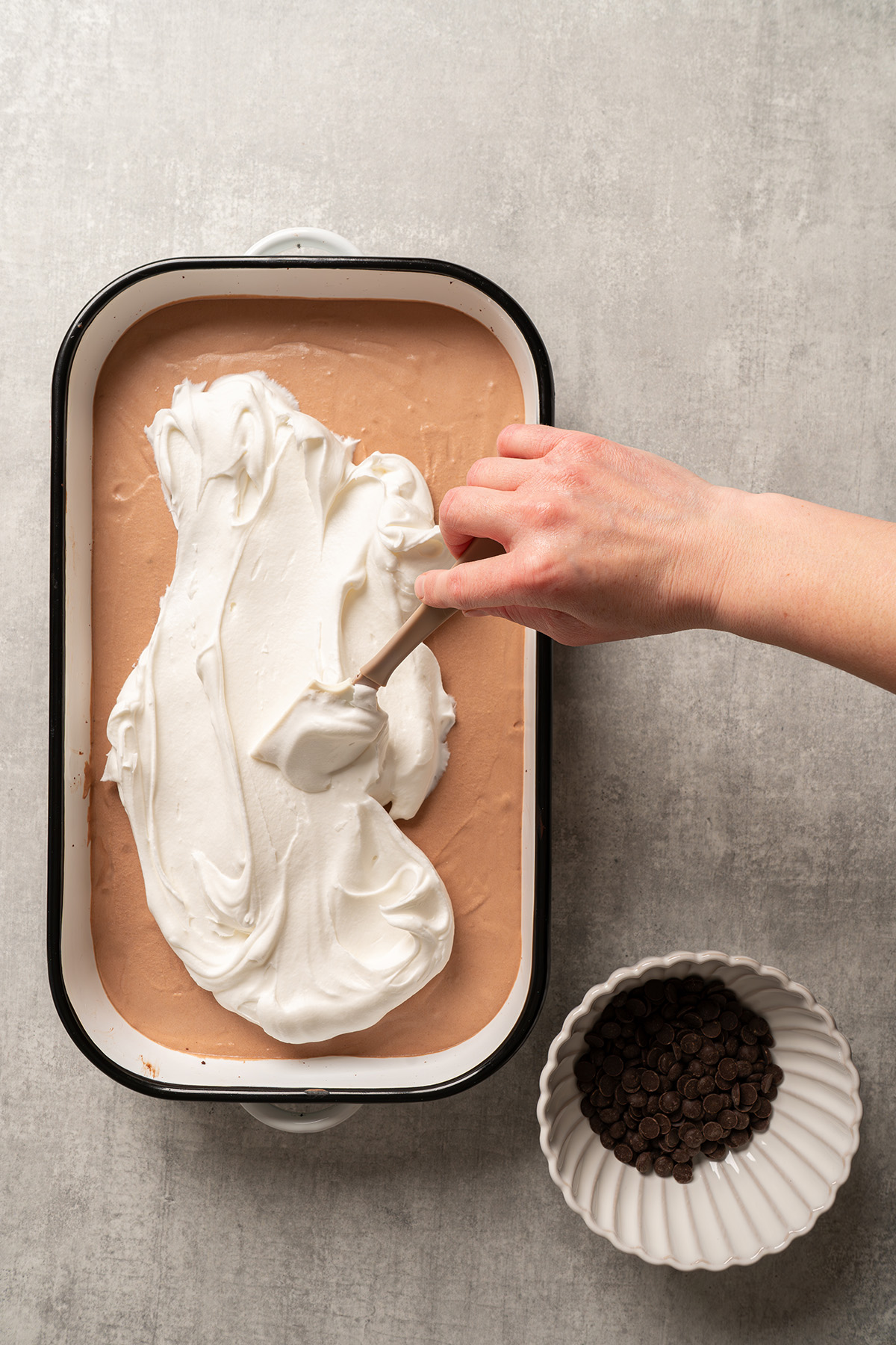 Whipped topping being spread over the chocolate silk layer on French silk brownies with brownie mix.