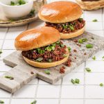 Korean sloppy joe sandwiches served on a stone board with glossy brioche buns and green onion garnish.