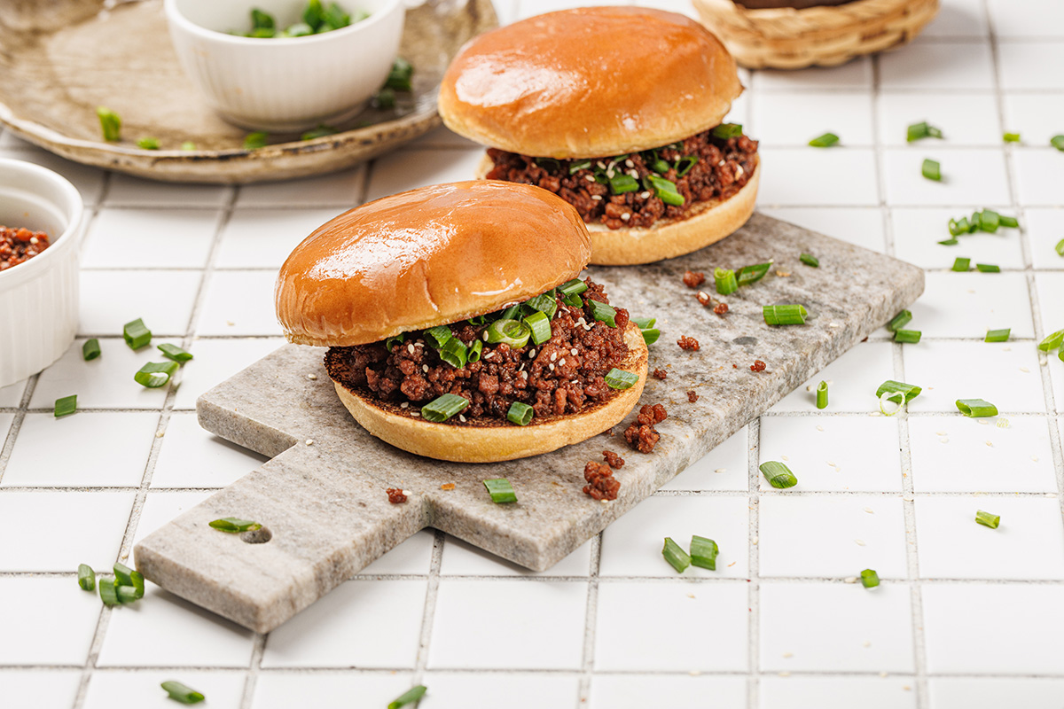 Korean sloppy joe sandwiches served on a stone board with glossy brioche buns and green onion garnish.