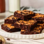Chocolate peanut butter box brownies stacked on a plate served with a glass of milk.