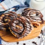 Chocolate brownie batter stuffed cinnamon rolls with icing and chocolate drizzle served on a wooden board with a glass of milk.