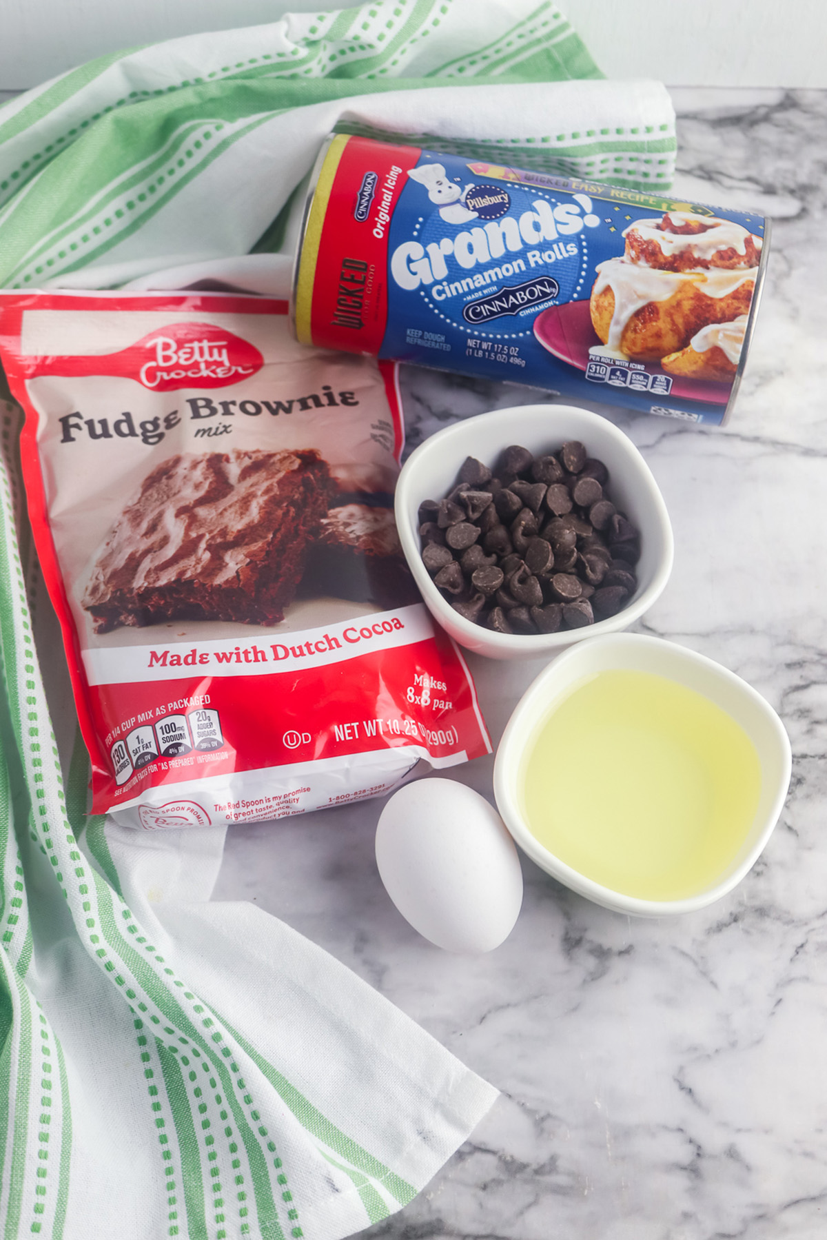 Ingredients for brownie cinnamon rolls including Pillsbury Grands cinnamon rolls, brownie mix, egg, vegetable oil, and chocolate chips.
