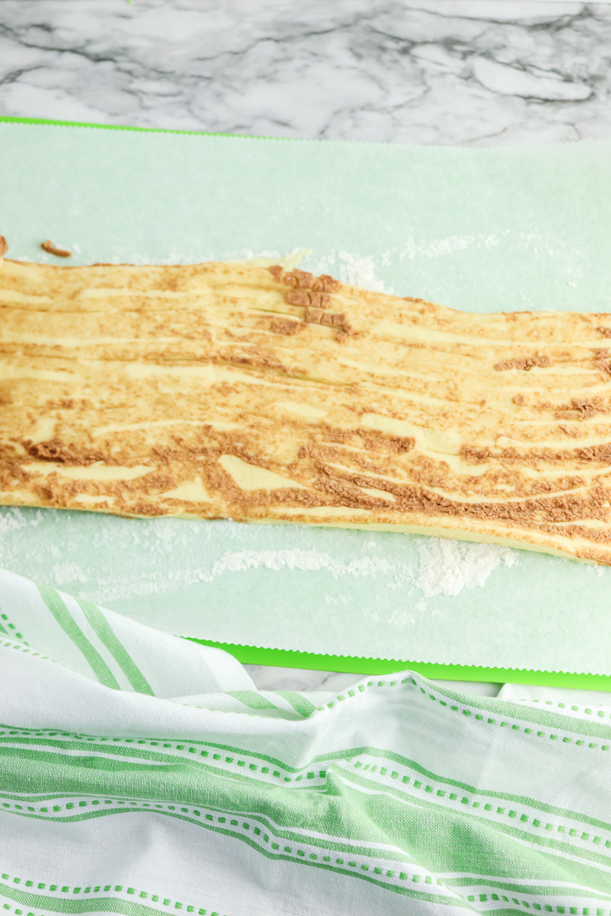 Unrolled cinnamon roll dough laid flat on parchment before adding brownie filling.