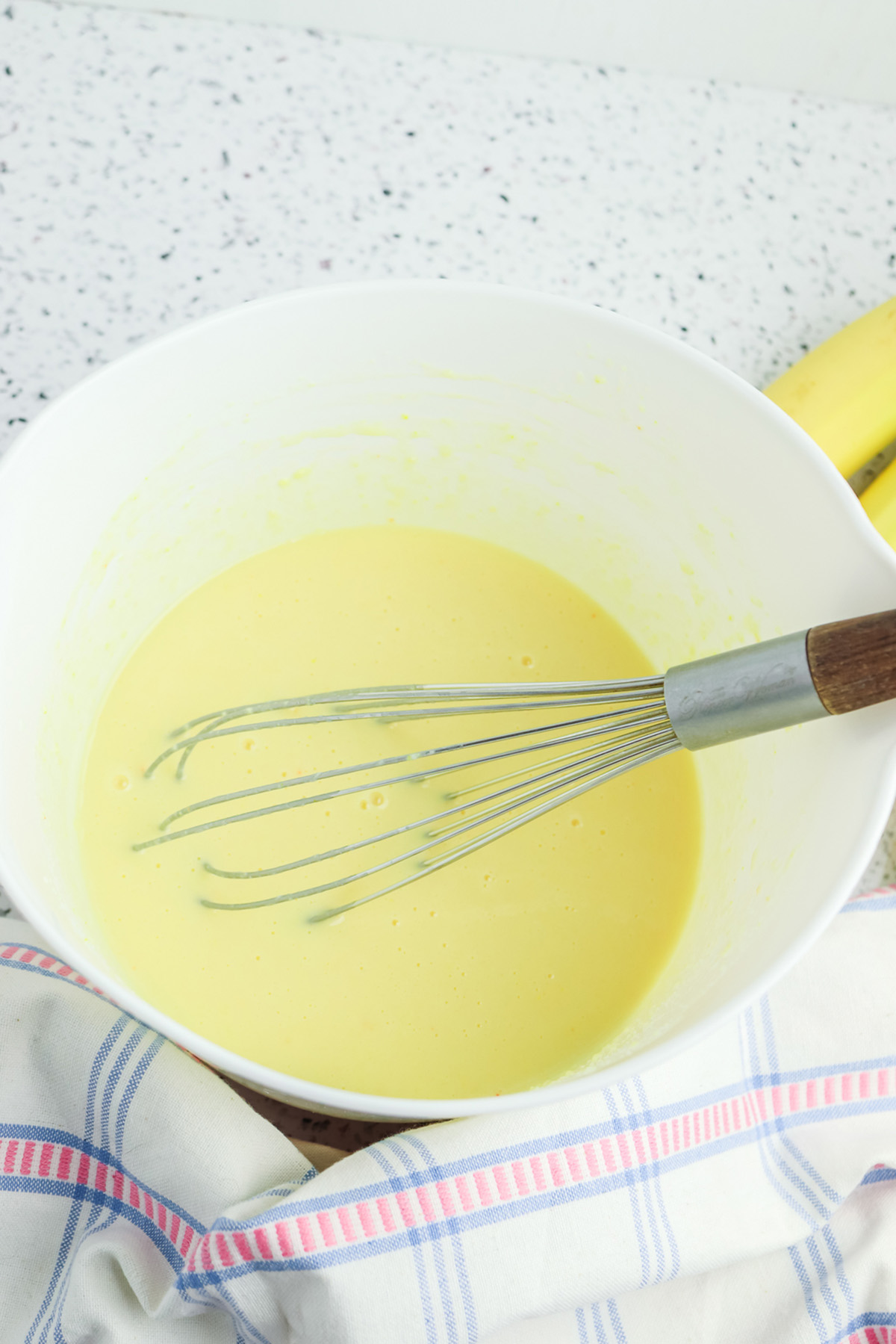 Whisking yellow vanilla pudding mixture in a white mixing bowl.