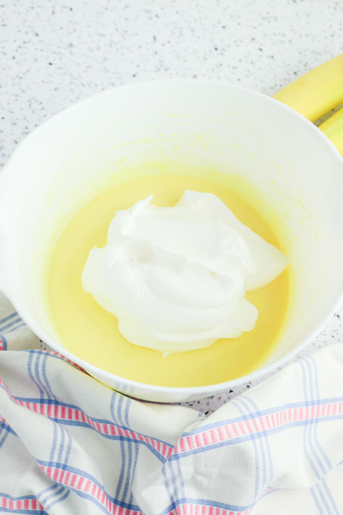 Whipped topping added to a bowl of prepared vanilla pudding mixture before folding together.