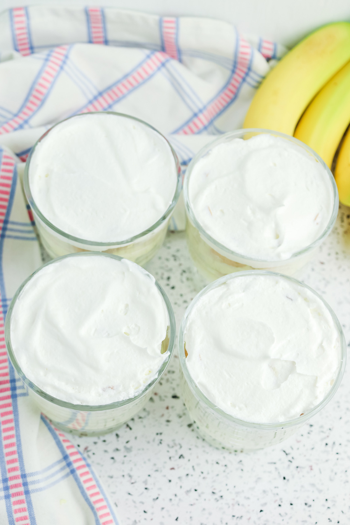 Four banana pudding cups topped with a smooth layer of whipped topping, ready to garnish.