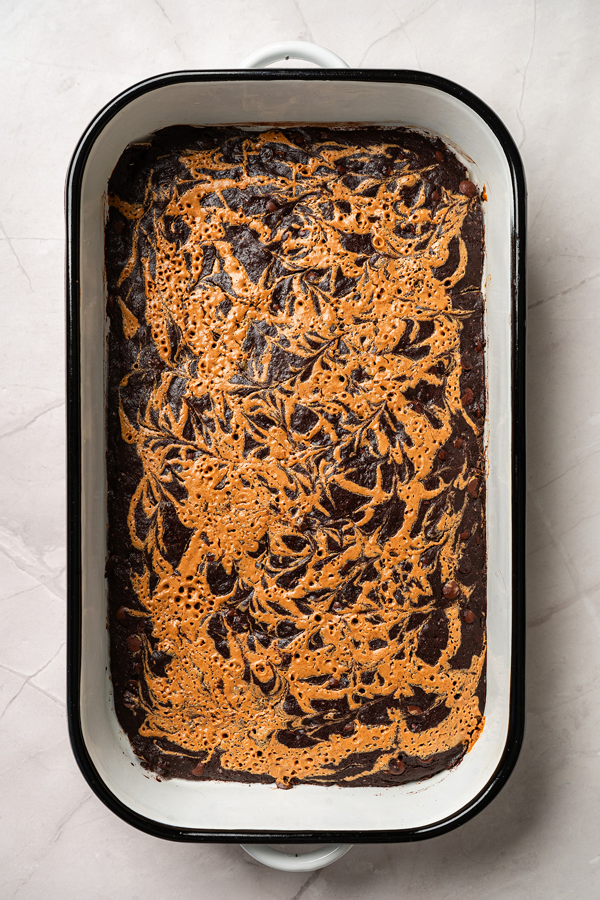 Freshly baked chocolate peanut butter swirl brownies in a 9x13 pan with golden peanut butter marbling on top.