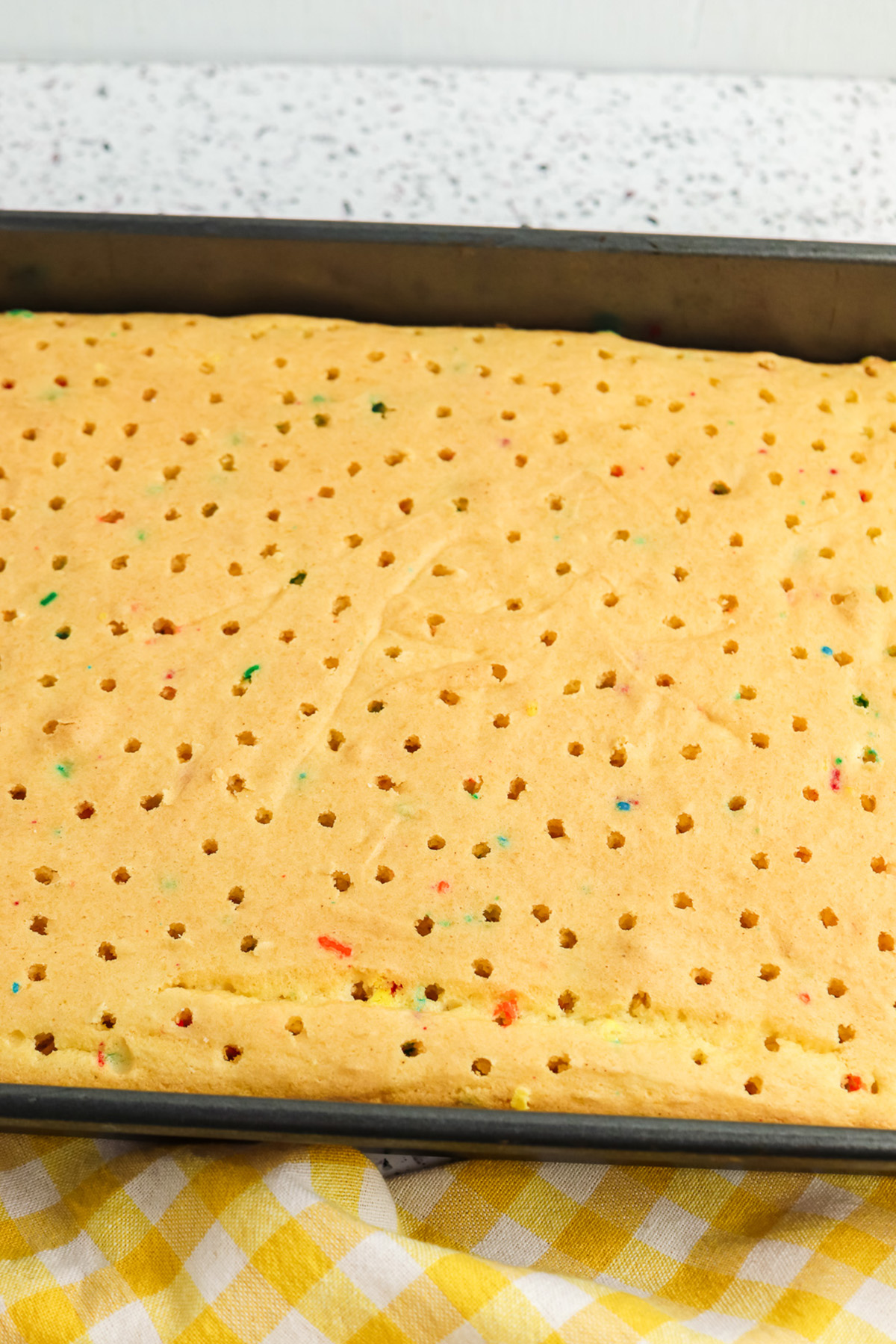 9x13 Funfetti cake poked all over with a fork for a rainbow poke cake recipe