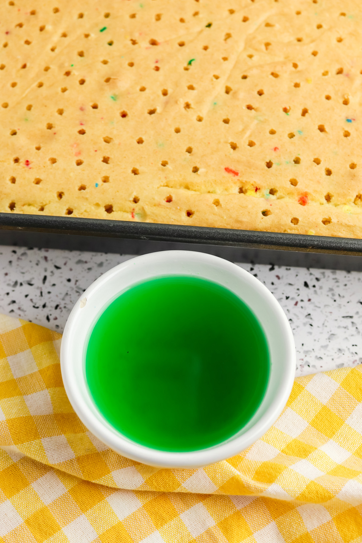 Poked Funfetti sheet cake with a bowl of green Jello mixture to fill the holes.
