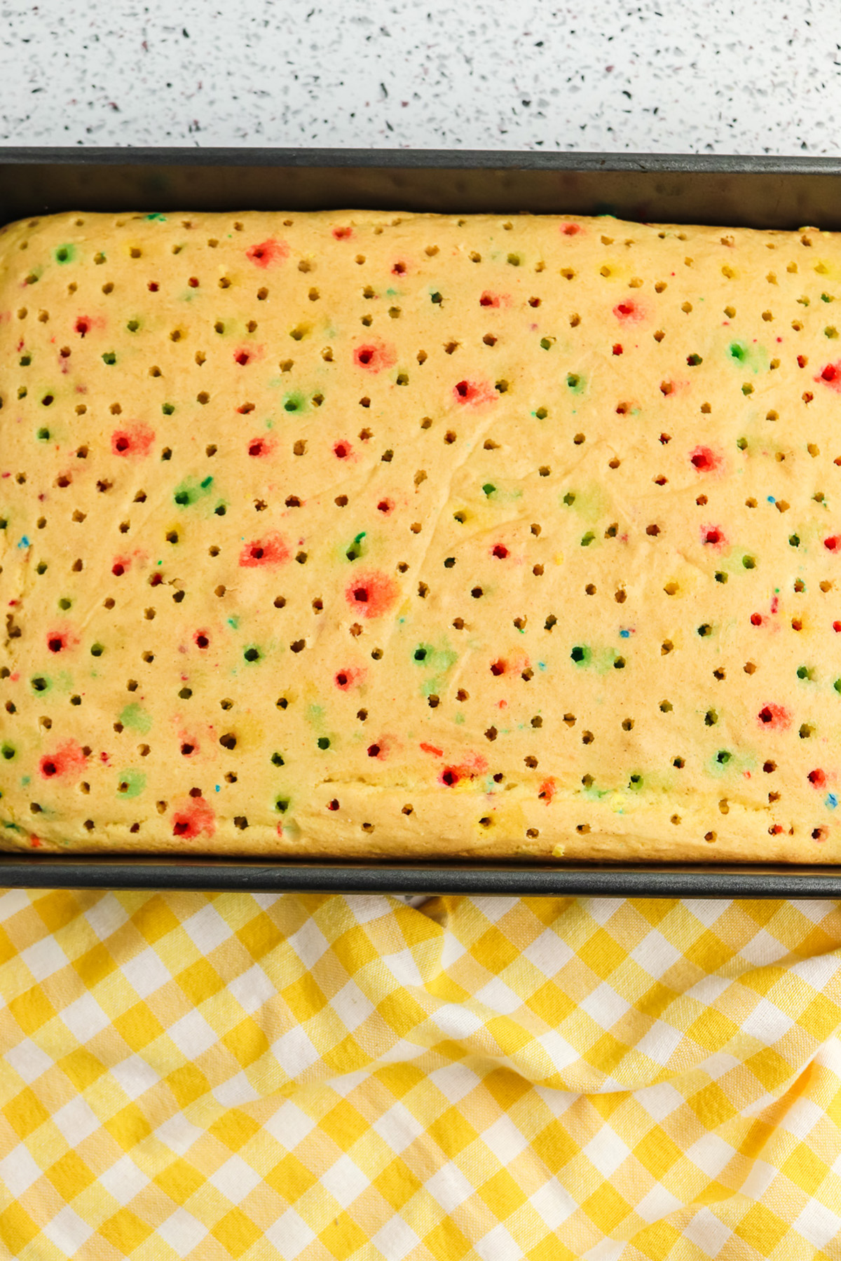 Funfetti sheet cake poked all over with holes in a 9x13 pan after adding Jello.