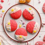 Overhead view of pink Easter cake mix cookies on a speckled plate, with white chocolate dipped cookies, crinkle cookies, pastel sprinkles, and speckled candy eggs.