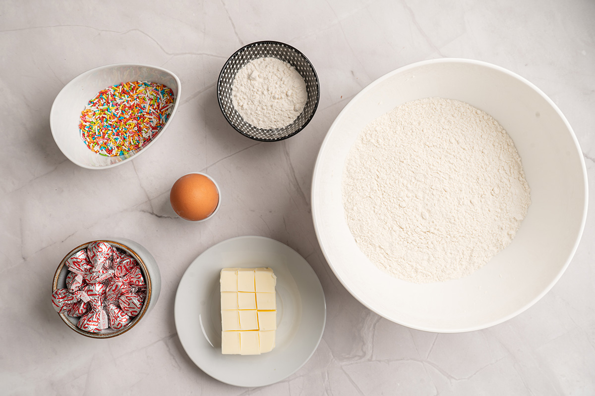 Ingredients for sugar cookie blossoms including sugar cookie mix, flour, butter, egg, rainbow sprinkles, and Hershey’s Hugs.