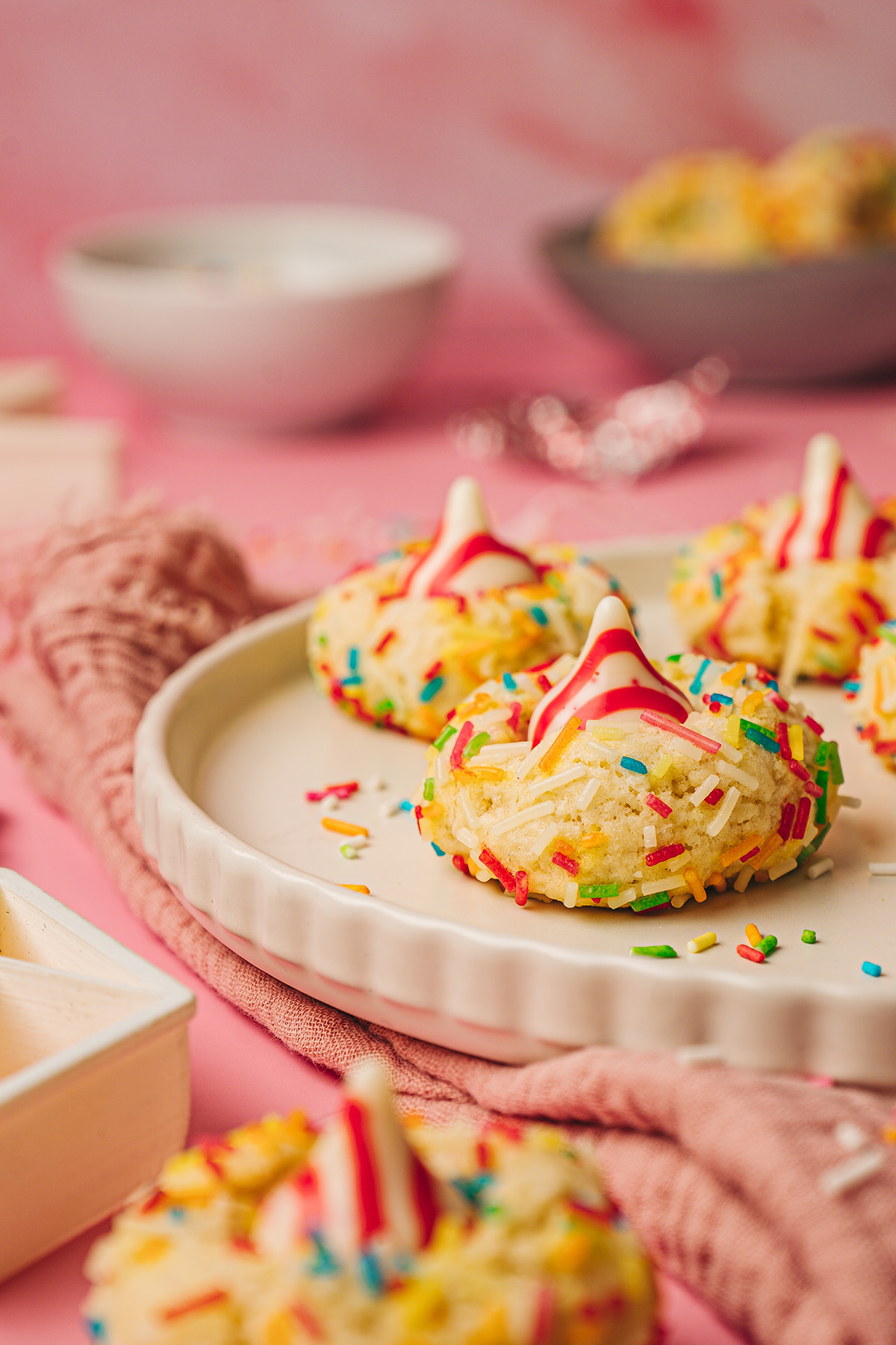 Sugar cookie blossoms on a scalloped plate with rainbow sprinkles scattered around on a pink surface.
