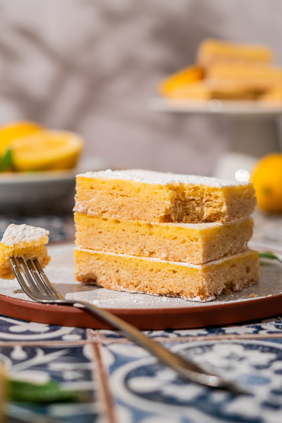 Easy sugar cookie lemon bars made with cookie mix crust, lemon juice, and zest. A sweet, tangy treat to chill and slice. Stack of sugar cookie lemon bars on a plate with a fork.