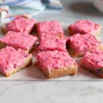 Frosted funfetti cookie bars cut into individual squares and slightly separated on parchment.