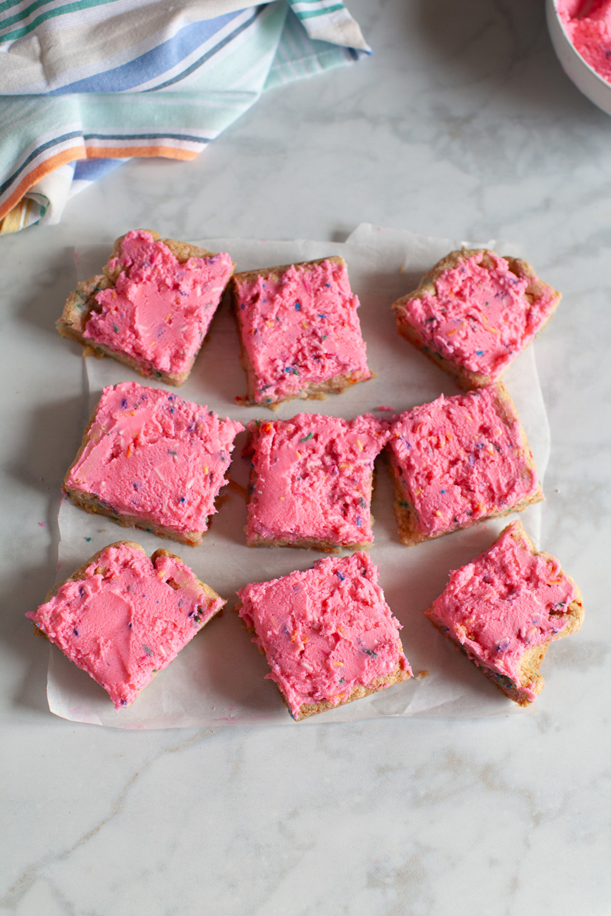 Funfetti sugar cookie bar squares arranged on parchment paper showing soft centers and frosted tops.
