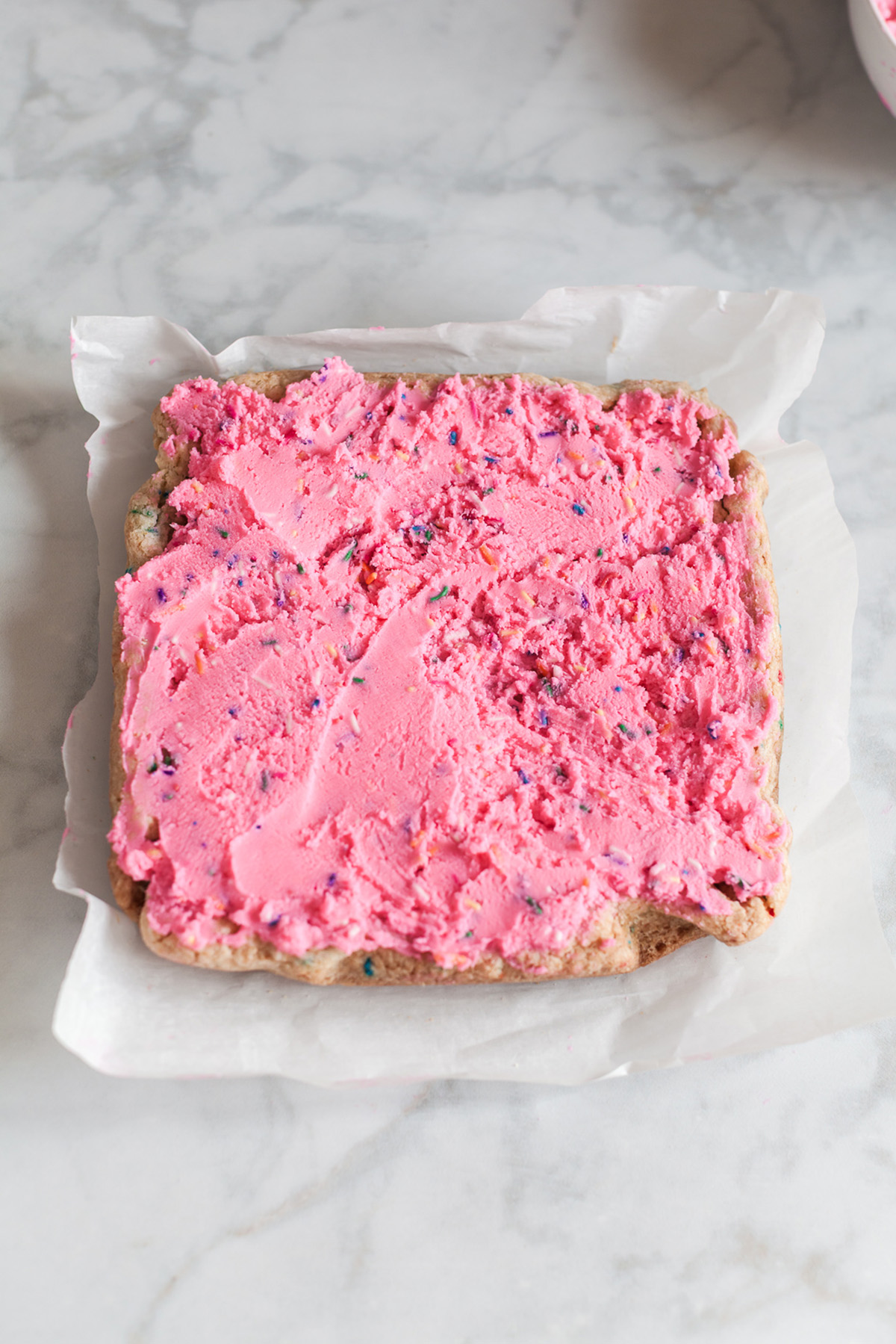 These funfetti sugar cookie bars start with a shortcut and bake up soft, buttery, and packed with sprinkles. Finished with a thick layer of pink frosting, they’re the kind of treat that disappears fast. Frosted funfetti sugar cookie bars spread with thick pink buttercream and rainbow sprinkles on parchment paper.