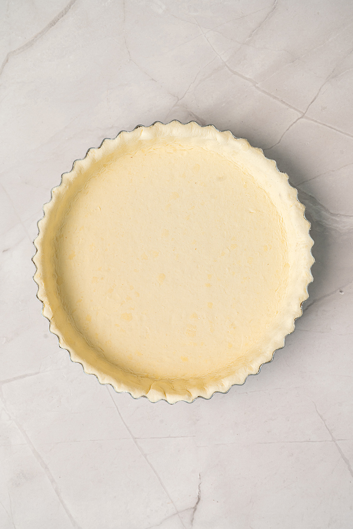 An empty unbaked pie crust pressed into a fluted tart pan, ready to be filled, on a marble countertop.