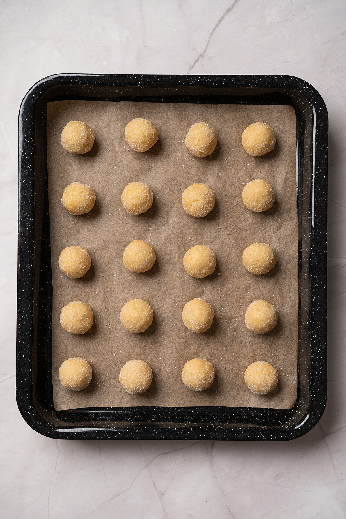 These cream cheese sugar cookies are soft, sweet, and topped with fluffy frosting. Starting with sugar cookie mix keeps them easy, but they still feel special enough for parties and holidays. Cream cheese sugar cookie dough rolled into sugar-coated balls and arranged on a parchment-lined baking sheet before baking.