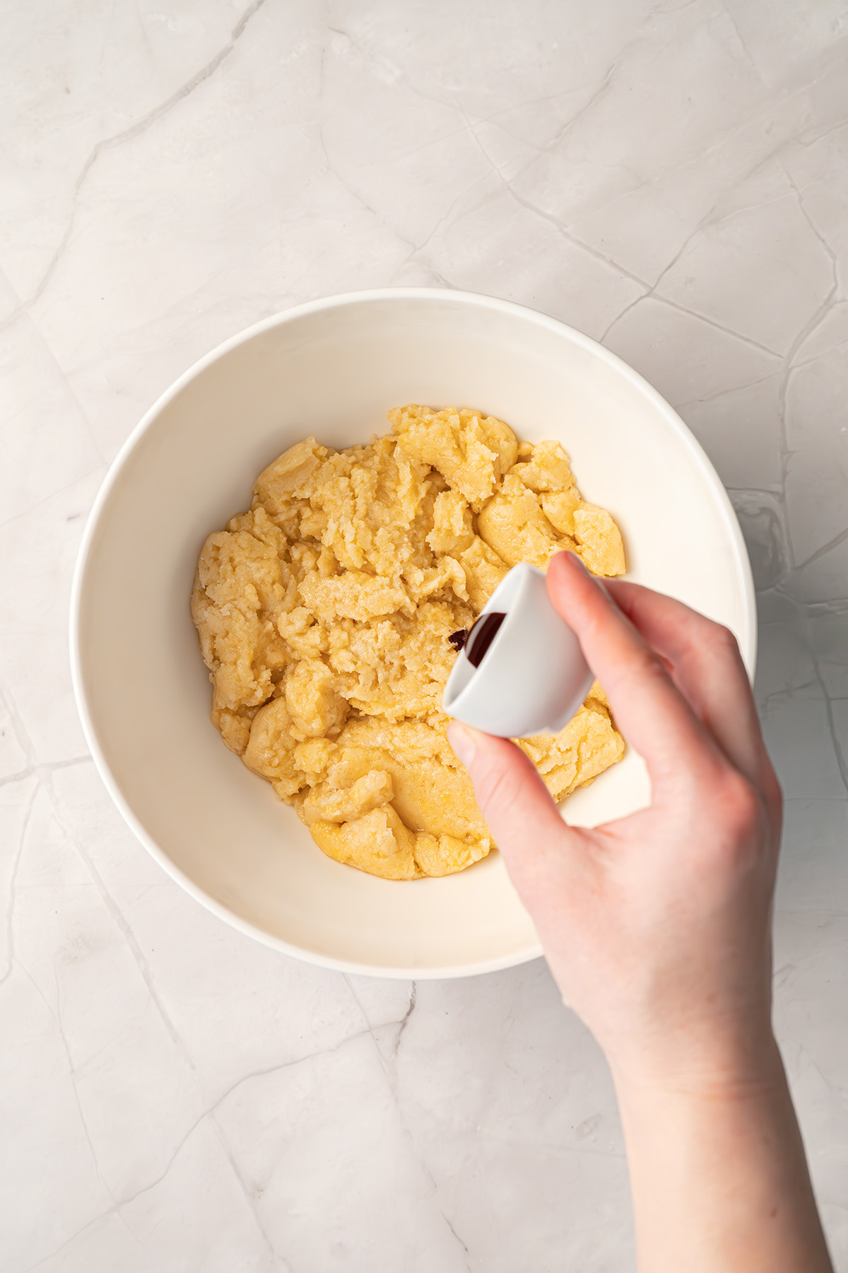 Hand pouring pink food coloring into a bowl of cookie dough.