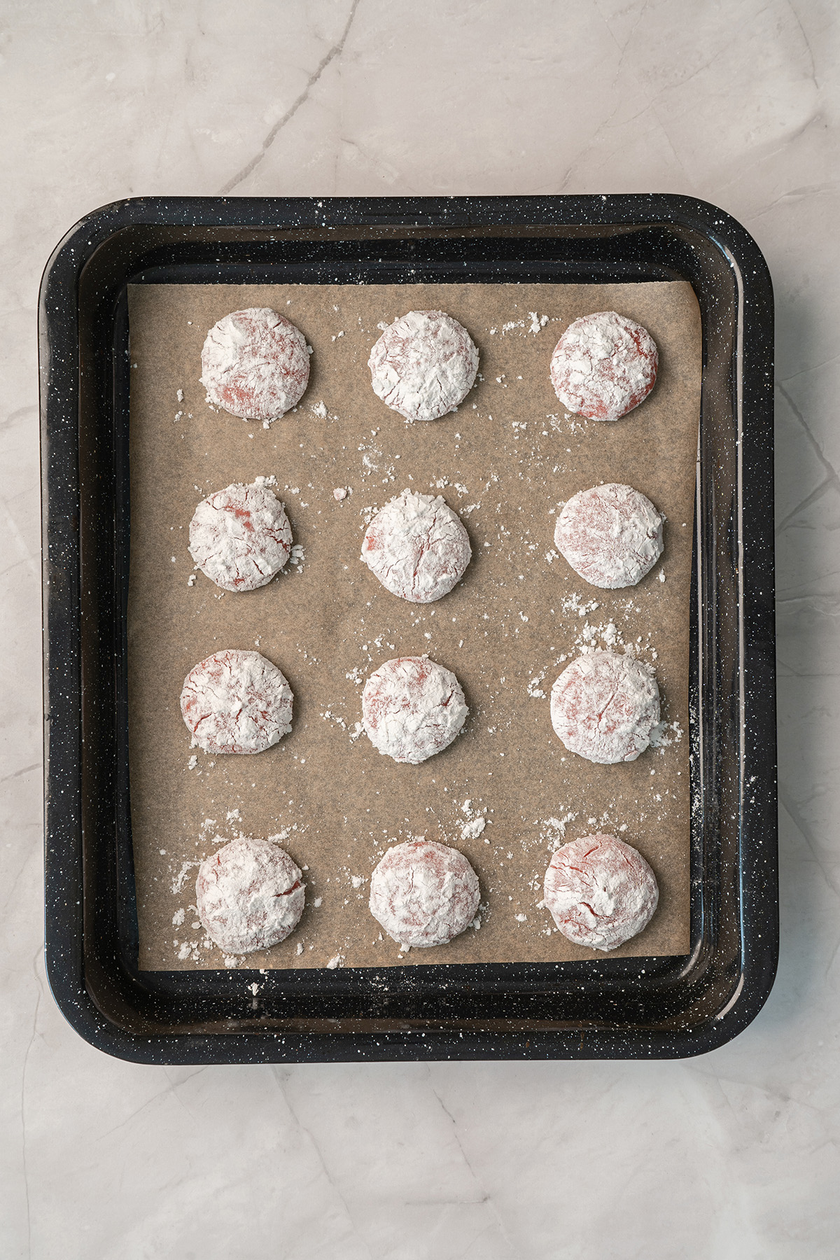Pink cake mix cookie dough balls coated in powdered sugar and arranged on a parchment-lined baking sheet before baking.