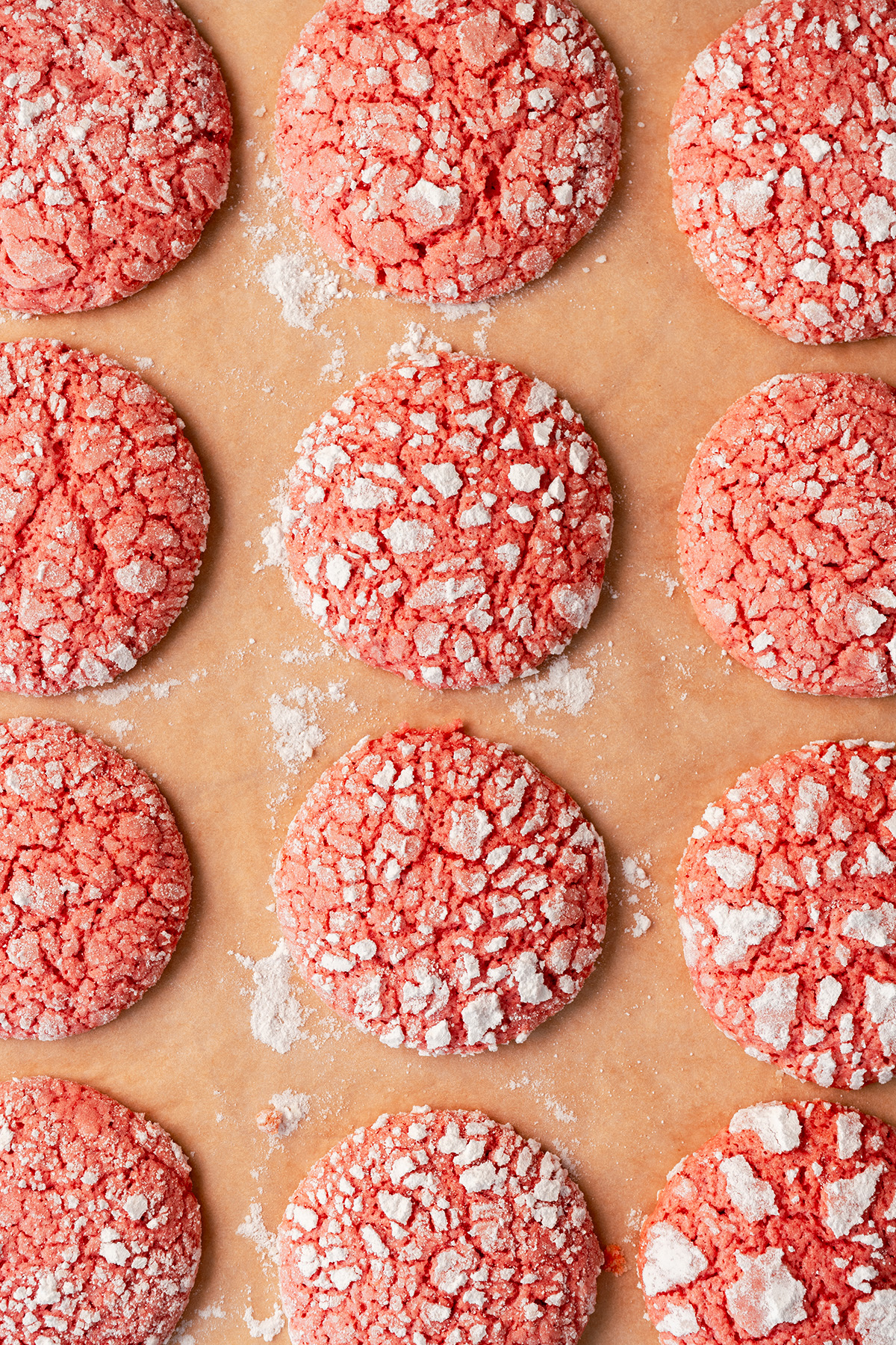 Pink cake mix crinkle cookies baked on parchment paper and dusted with powdered sugar.