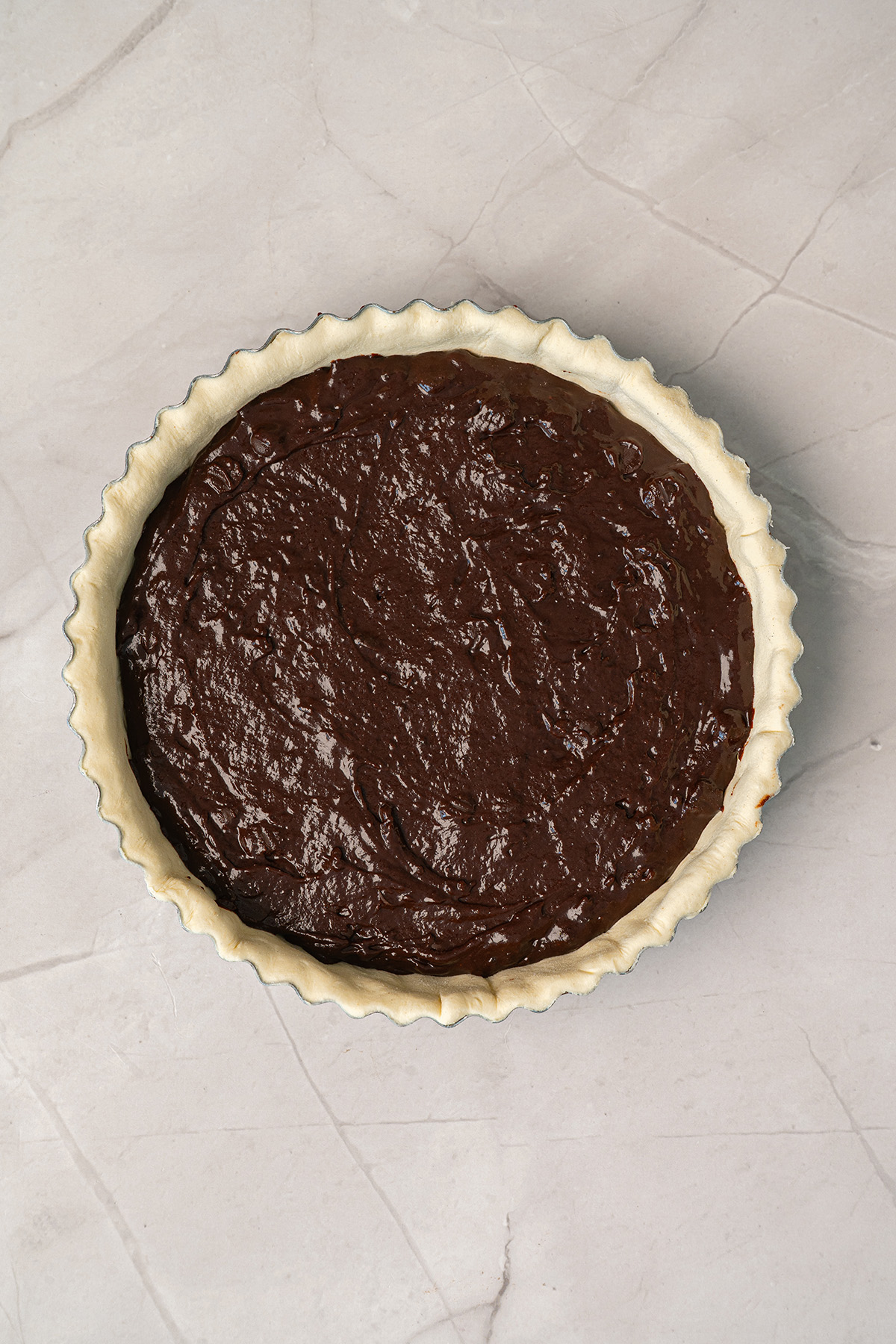 Unbaked brownie pie showing thick, glossy chocolate brownie batter spread evenly into a raw pie crust in a fluted tart pan, viewed from above.