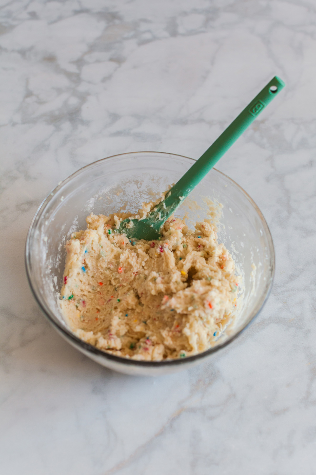 These funfetti sugar cookie bars start with a shortcut and bake up soft, buttery, and packed with sprinkles. Finished with a thick layer of pink frosting, they’re the kind of treat that disappears fast. Thick funfetti cookie dough mixed in a glass bowl with rainbow sprinkles visible throughout.