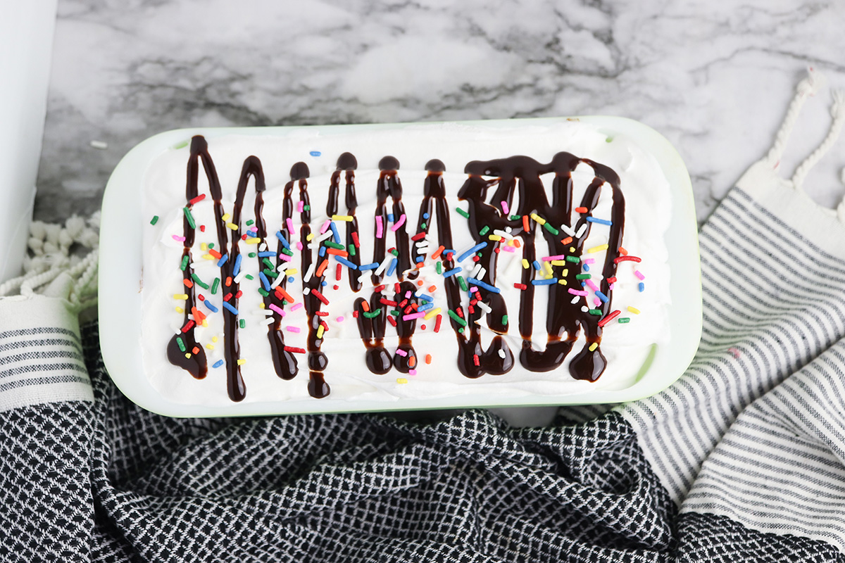 Klondike ice cream cake topped with whipped topping, chocolate syrup, and rainbow sprinkles before slicing.