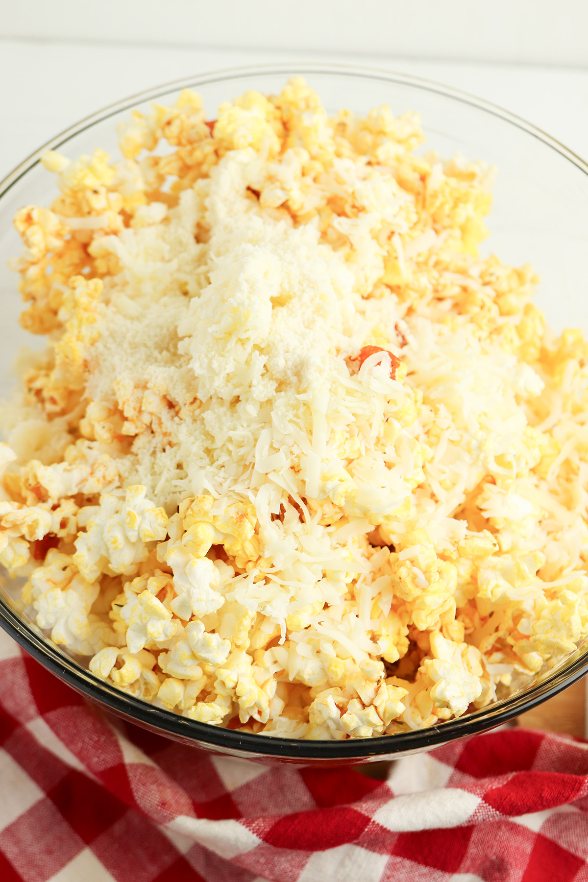 Shredded pizza blend cheese and grated parmesan sprinkled over the buttery pepperoni popcorn in a glass bowl, before being tossed together.