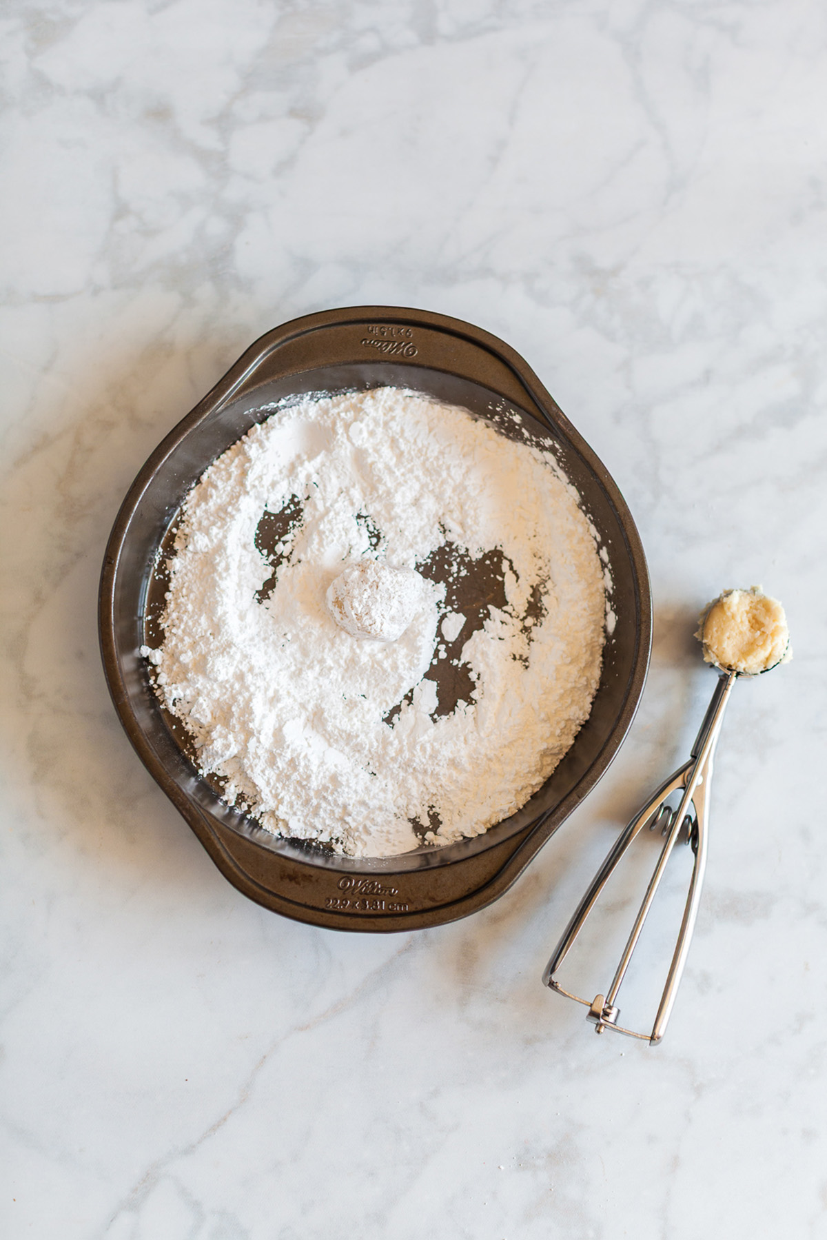 Cookie dough ball being rolled in powdered sugar mixture for vanilla cake mix crinkle cookies.