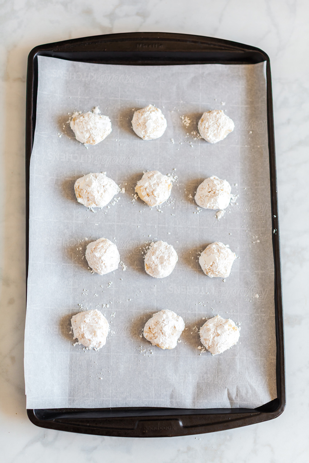 Powdered sugar coated vanilla cake mix cookie dough balls spaced on a baking sheet before baking.