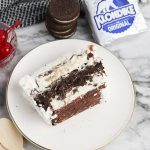 Klondike ice cream cake slice on a plate with cherries, Oreo cookies, and Klondike bars in the background.