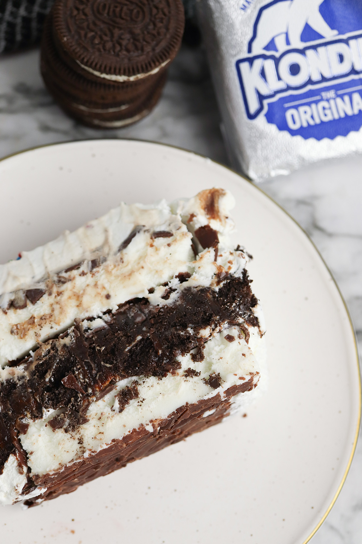 Close-up of a slice of Klondike ice cream cake showing layers of vanilla ice cream, Oreo fudge filling, whipped topping, and chocolate coating.