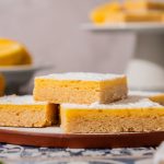 Sugar cookie lemon bars stacked on a plate, dusted with powdered sugar.