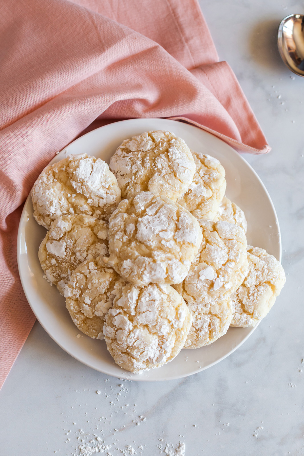 Easy vanilla cake mix crinkle cookies on a plate with a pink cloth, featuring soft centers and powdered sugar cracks.