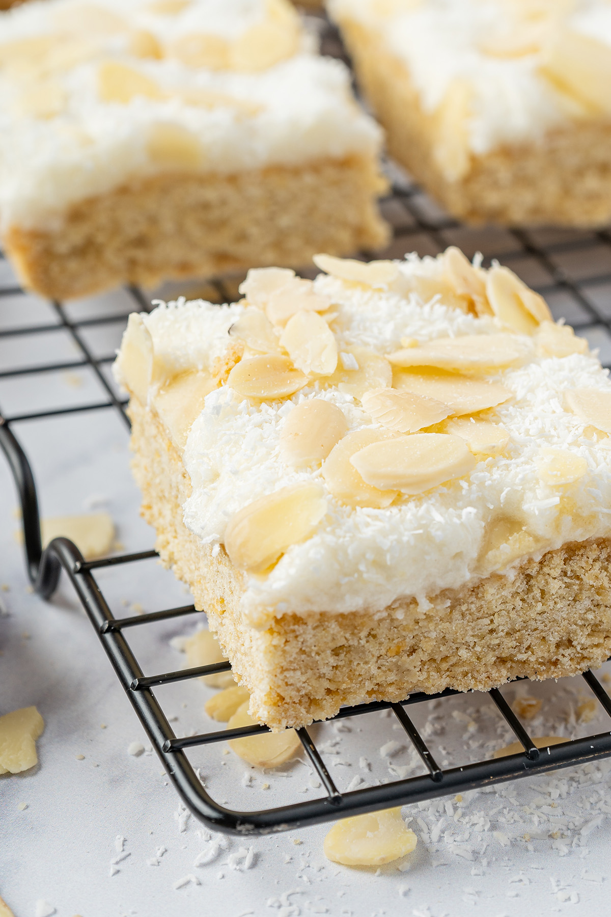 Close-up of a frosted coconut sugar cookie bar with fluffy coconut frosting and sliced almonds.