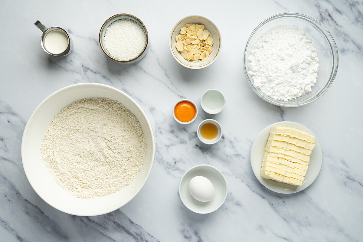 Ingredients for coconut sugar cookie bars including flour, butter, eggs, coconut, powdered sugar, and vanilla.