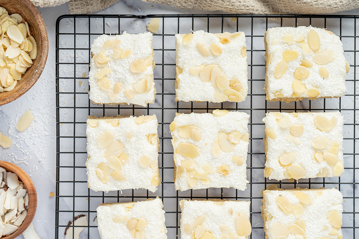 Close overhead of coconut sugar cookie bars with creamy frosting, coconut, and sliced almonds.