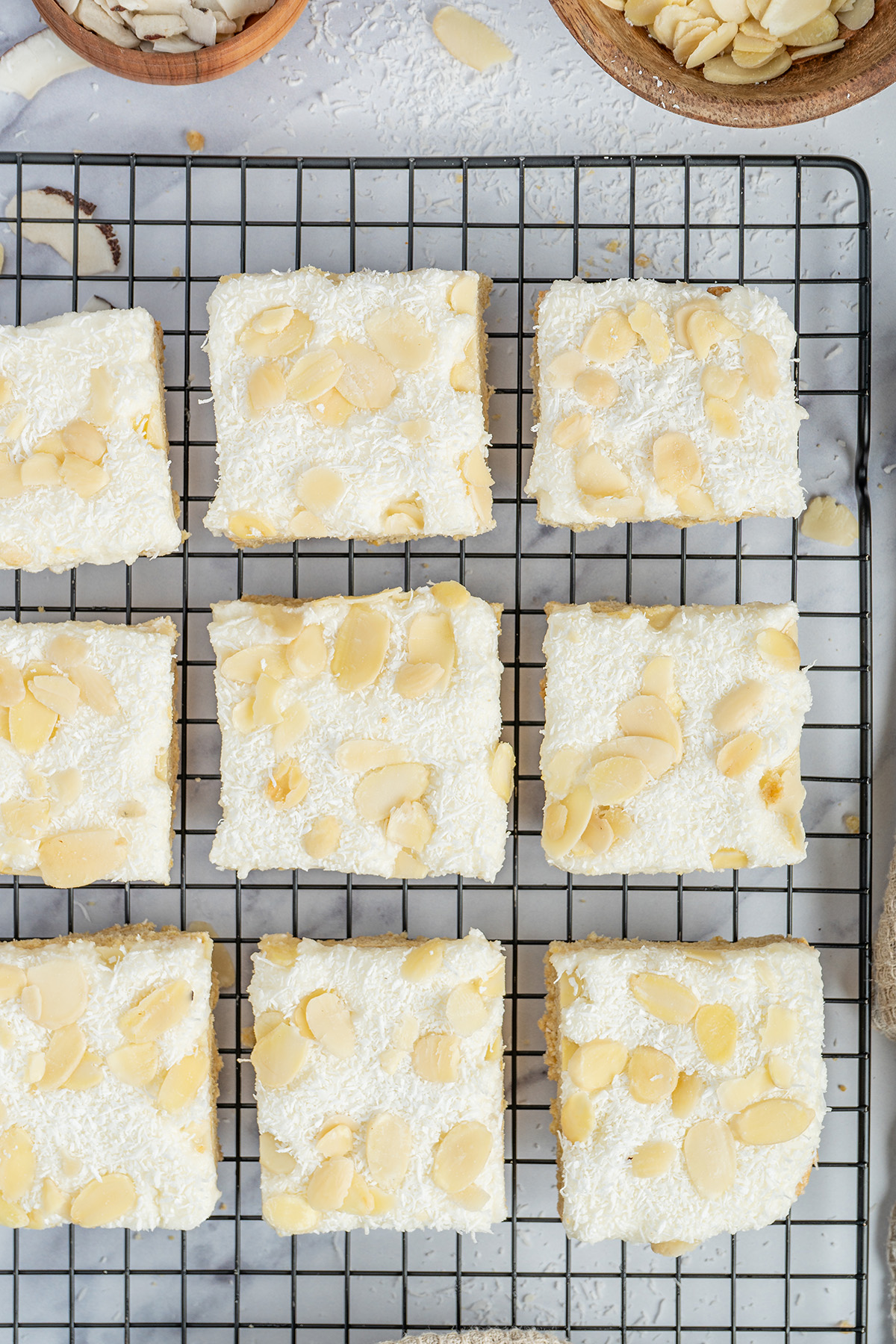Overhead view of frosted coconut sugar cookie bars topped with shredded coconut and almond slices.