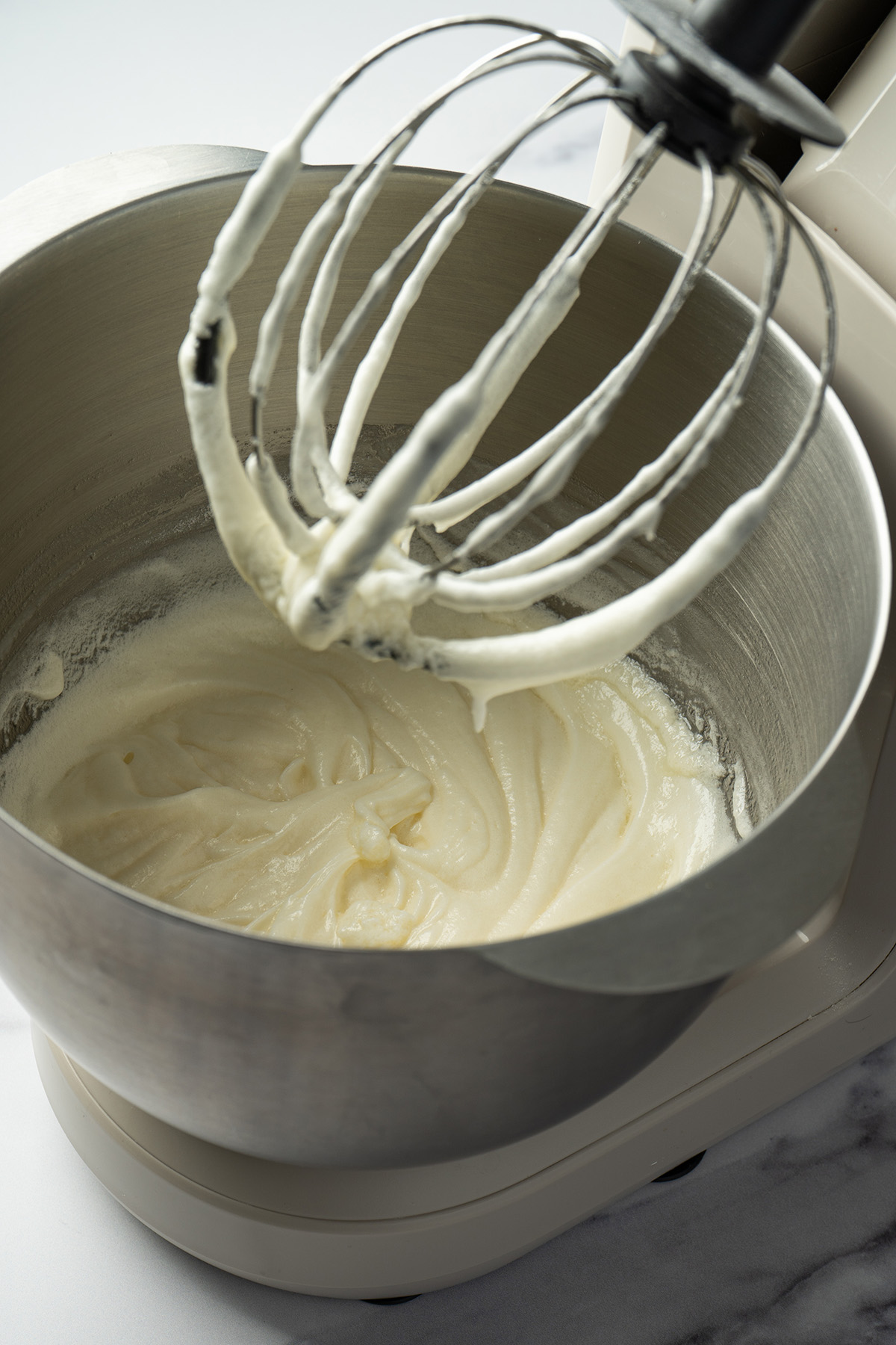 Creamy coconut frosting being whipped in a stand mixer for frosted coconut sugar cookie bars.