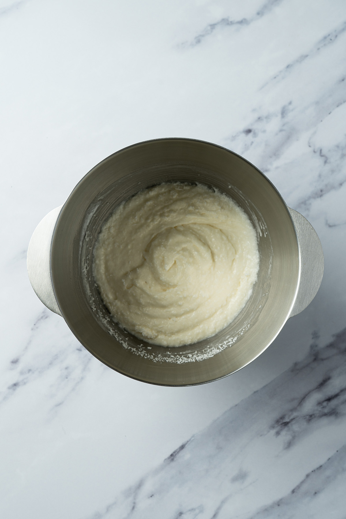 Fluffy coconut frosting in a mixing bowl, ready to spread on sugar cookie bars.