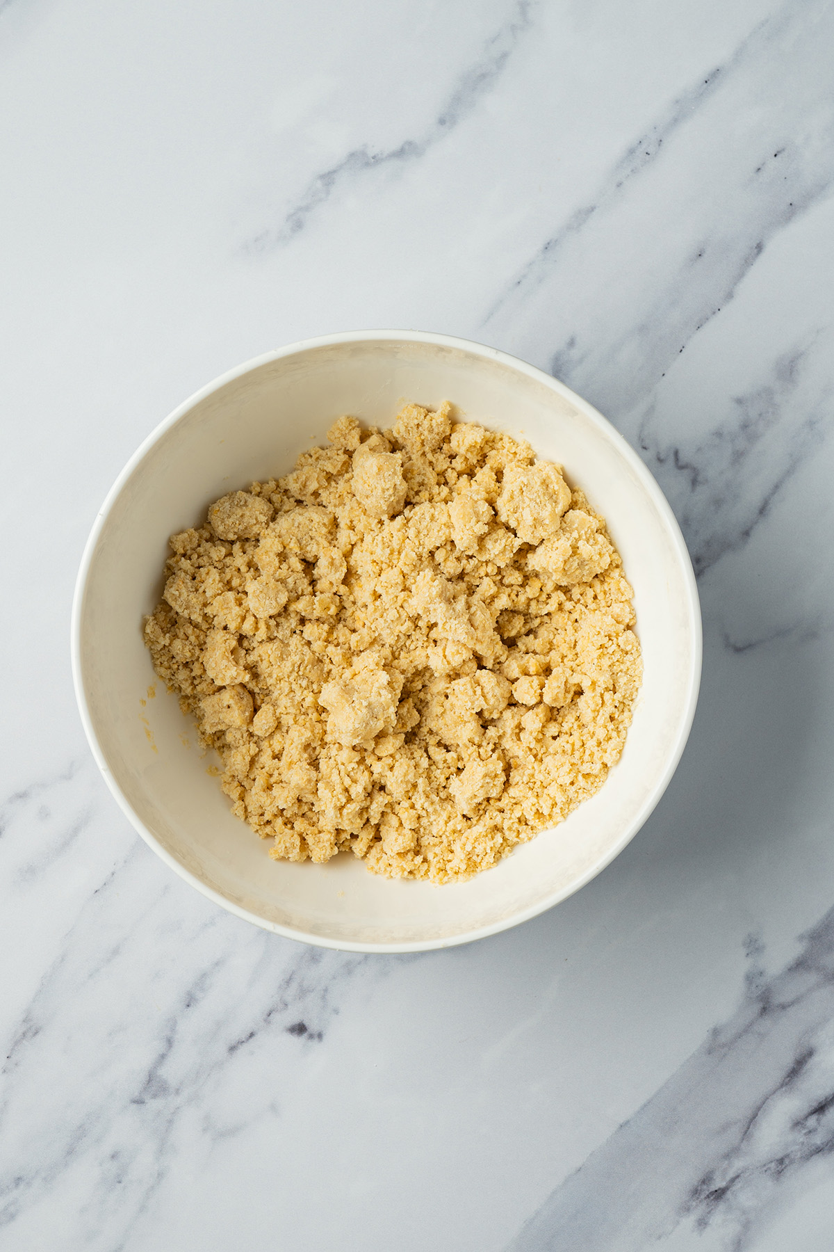 Coconut sugar cookie bar dough mixture with a crumbly texture in a white mixing bowl.