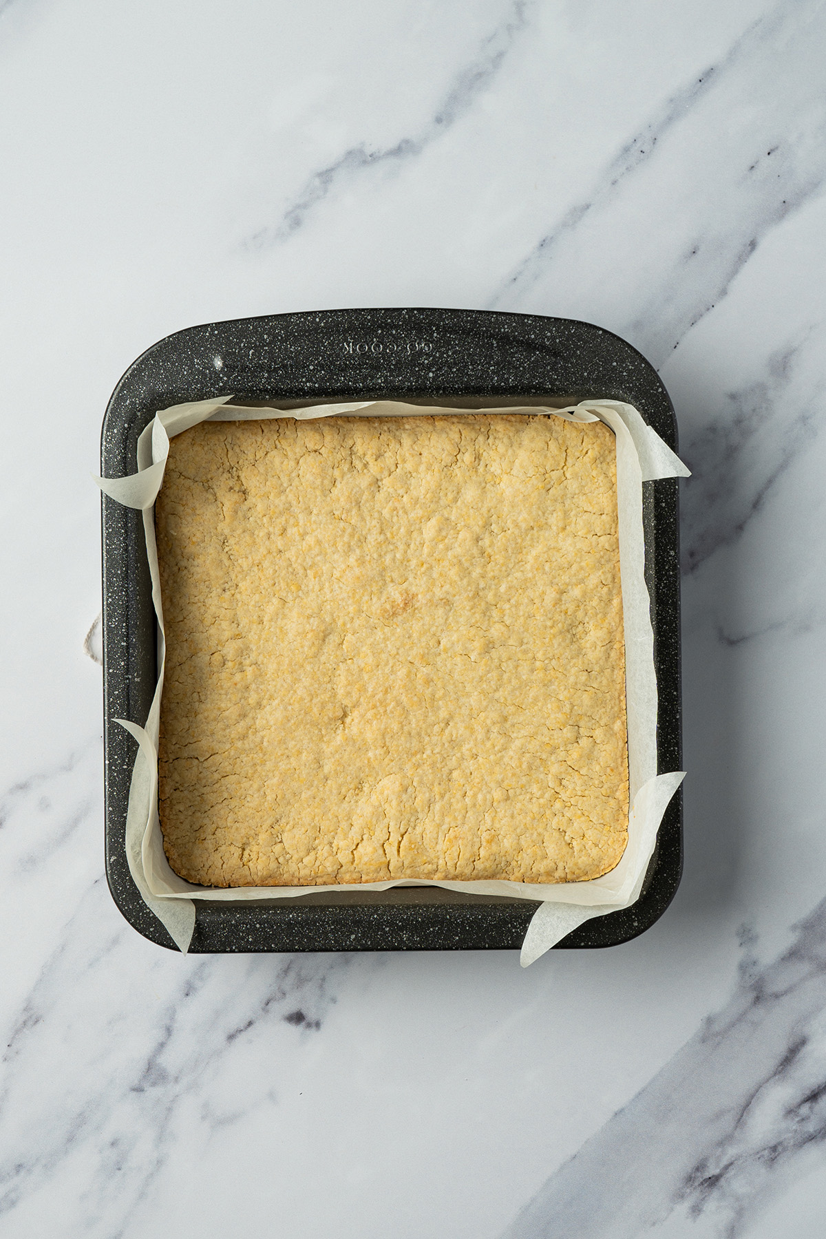 Baked sugar cookie bar base in a parchment-lined square pan, lightly golden and ready to frost.