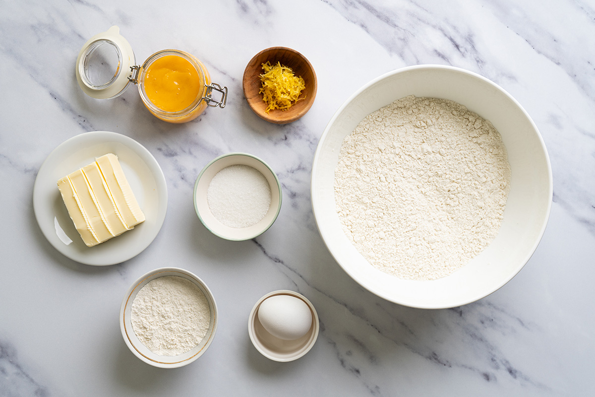 Ingredients for lemon thumbprint cookies including flour, butter, egg, sugar, and lemon zest in a mixing bowl.